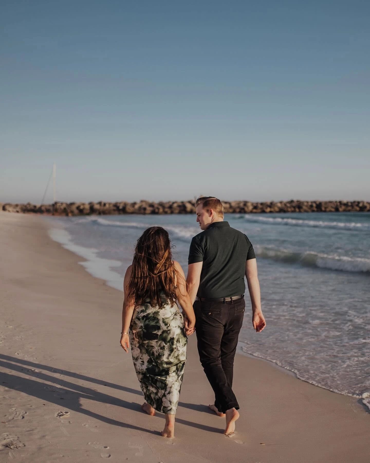 Allison and Daniel walking hand in hand along the shoreline at sunset